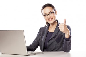Smiling business woman showing thumbs up next to her laptop